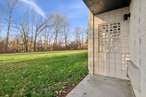 Boise apartment for rent - A concrete building with a window and a door is in the foreground with a grassy field and trees in the background.