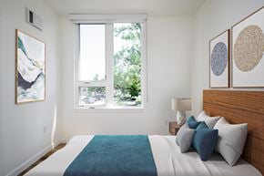 Gresham apartment for rent - The Wes Gresham Oregon Apartments A bedroom with a large bed and a window overlooking a tree-filled street.