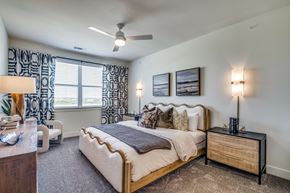 Lewisville apartment for rent - A bedroom with a large bed, a nightstand with a lamp, and a ceiling fan.