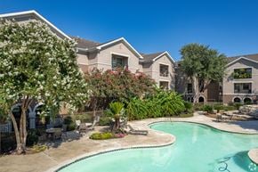 Houston apartment for rent - A swimming pool surrounded by a landscaped garden and residential buildings.