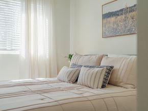 Lacey apartment for rent - A bed with a white comforter and striped pillows with a plant on it.