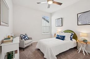 Pflugerville apartment for rent - A bedroom with a white bed and a grey armchair.