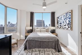 Dallas apartment for rent - A bedroom with a large bed and a city view through the window.