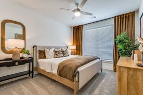 Mckinney apartment for rent - A bedroom with a bed, a mirror, a nightstand, and a plant.