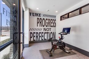 Lewisville apartment for rent - A gym with a wall that says "I like progress not perfection" and a stationary bike in front of it.