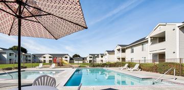 Yakima apartment for rent - A pool surrounded by chairs and umbrellas with apartment buildings in the background.