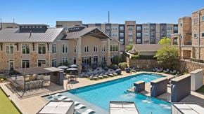 Garland apartment for rent - A large swimming pool surrounded by lounge chairs and umbrellas in front of a building.