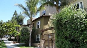 San Diego apartment for rent - A house with a brown fence and a gate is surrounded by green trees.