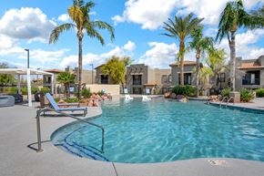 Tucson apartment for rent - A pool surrounded by palm trees and a building in the background.