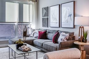 Milwaukee apartment for rent - A modern living room with a grey couch, a glass table, and a large window with blinds.