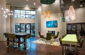 Atlanta apartment for rent - Resident lounge area with multiple tables to sit at, a mounted TV, and a door to the pool area. 