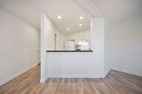 Carlsbad apartment for rent - the living room and kitchen of an apartment with white walls, vinyl wood flooring, white appliances, and a breakfast bar.