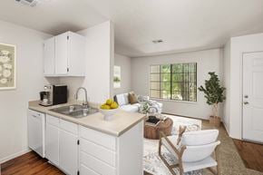 Kingman apartment for rent - Carpeted living room and kitchen with wood-style vinyl plank flooring, white cabinets, and large window.