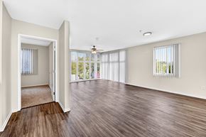 San Diego apartment for rent - Apartment living room with wood-style plank flooring, ceiling fan, huge floor-to-ceiling windows, and view to bedroom.