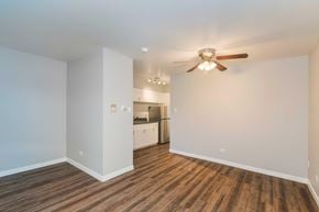 Denver apartment for rent - A room with a ceiling fan and wooden flooring with a kitchen in the background.