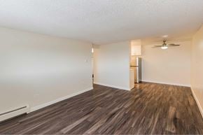 Denver apartment for rent - A room with wooden style flooring and a ceiling fan with a peak view of a kitchen in the background.