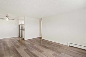 Denver apartment for rent - A room with a wooden floor and a ceiling fan and a kitchen with a fridge in the background.