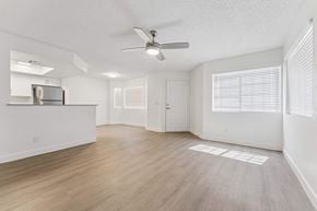 Glendale apartment for rent - Apartment interior living room area with light brown vinyl flooring, ceiling fan, white walls, and slight view of kitchen counter and dining room area.