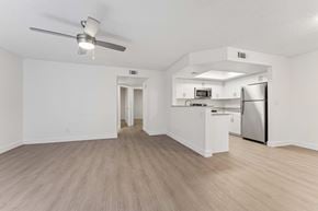 Glendale apartment for rent - Apartment interior living room area with light brown vinyl flooring, ceiling fan, white walls, and slight view of kitchen counter and dining room area.