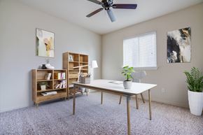 Coalinga apartment for rent - A bedroom with carpet, a ceiling fan, and a window with blinds. The room is staged as an office with shelving, a desk, and a chair.
