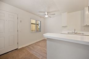 Oceanside apartment for rent - The kitchen and living room with a white counter tops, a ceiling fan, and a window.