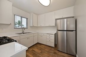 Oceanside apartment for rent - A kitchen with white cabinets, a stainless steel refrigerator, and a window above the sink.