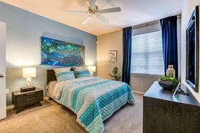Orlando apartment for rent - Model apartment bedroom with a bed, nightstand, and a painting on the wall.