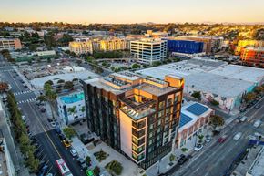 San Diego apartment for rent - A modern building is surrounded by other buildings and busy streets.