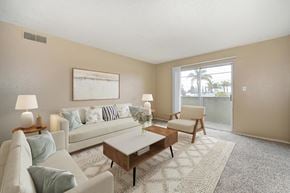 Ceres apartment for rent - A living room with beige walls, a sliding glass door to a balcony, and carpet the room is staged with a couch, a wooden coffee table, and artwork on the wall.
