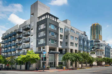 San Diego apartment for rent - A modern building with a grey facade and balconies is situated on a street with trees and other buildings in the background.
