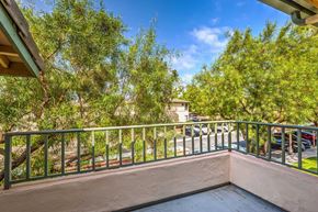 Bonita apartment for rent - A balcony with a green railing overlooks a parking lot and trees.
