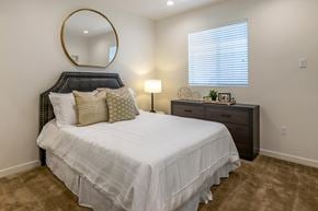 Anaheim apartment for rent - A bedroom with brown carpet, a large bed, a window, and a round mirror on the wall.