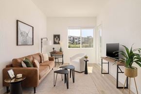 Fort Collins apartment for rent - A living room with a brown couch, a white chair, and a TV on a stand.