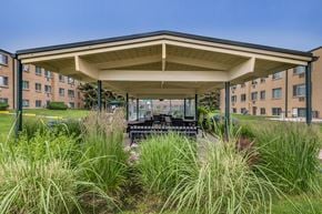 Greeley apartment for rent - A covered patio area with a table and chairs in front of apartment buildings.