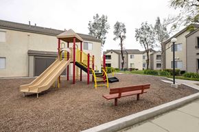 Hemet apartment for rent - A playground with a yellow and red slide, a wooden swing set, and a red bench.