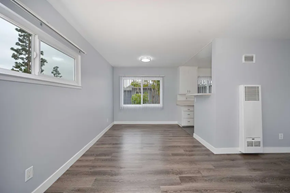 Inglewood apartment for rent - Bright and spacious room with light gray walls, large window with blinds, and modern wood flooring. The area features a ceiling light fixture and an open layout that connects to a kitchen or dining space, with a small wall-mounted heater on one side. Ideal for creating a cozy living environment.