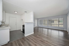 Inglewood apartment for rent - A modern kitchen area with white cabinets and a gas stove, featuring an open layout that connects to a spacious living area. Large windows with vertical blinds allow natural light to fill the room. The flooring is a sleek, light-colored laminate.