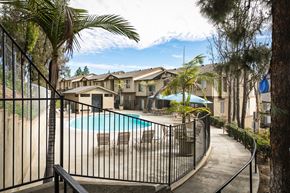 Lakeside apartment for rent - A pool surrounded by a black fence with palm trees in the background.