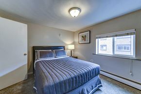 Lakewood apartment for rent - A bedroom with a bed, a nightstand with a lamp, and a window.