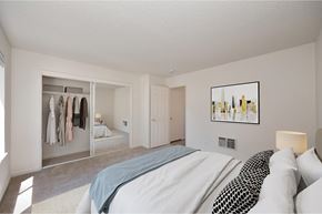 Modesto apartment for rent - A bedroom with carpet, white walls, and a sliding mirrored closet door. The room is staged with clothes in the closet, a bed, and a rug.