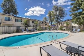 Fresno apartment for rent - A swimming pool surrounded by lounge chairs and the apartment building.