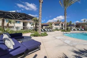 Fresno apartment for rent - A poolside area with lounge chairs and palm trees.