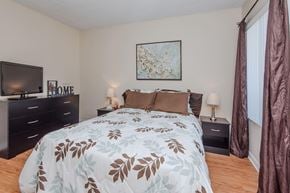 Ventura apartment for rent - A bedroom premium wood style flooring, beige walls, and a window. The room is staged with a bed, nightstands, a television, and a painting on the wall.