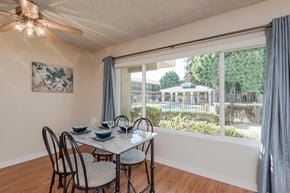 Ventura apartment for rent - The dining room area with a large window that looks out to the pool area, premium wood style flooring, and a ceiling fan with a light. The area with stage with curtains, a table, and 4 chairs.