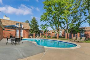 Greeley apartment for rent - A pool surrounded by a patio area and chairs within a brick apartment complex.