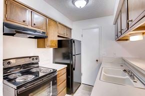 Greeley apartment for rent - A kitchen with a black refrigerator, stove, wood cabinets, and oven.