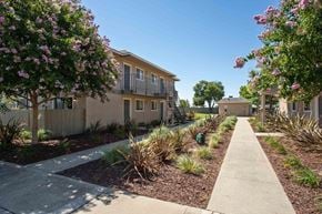 Ceres apartment for rent - The sidewalk in between the apartment buildings with bark, bushes, and trees.