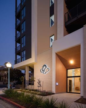 San Diego apartment for rent - A modern building with a wooden entrance and a sign with a stylized flower.