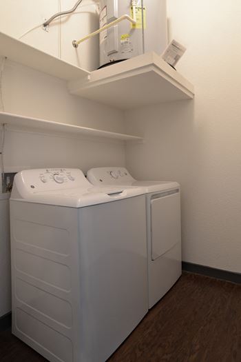 A white washer and dryer in a room with a shelf on the wall