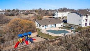 Caldwell apartment for rent - A playground with a red slide is in front of a building with a pool.